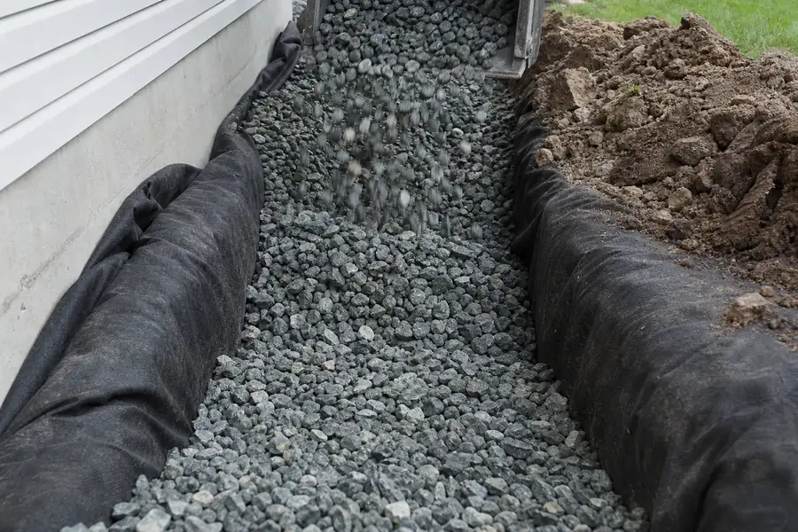 French drain trench being filled with #57 stone