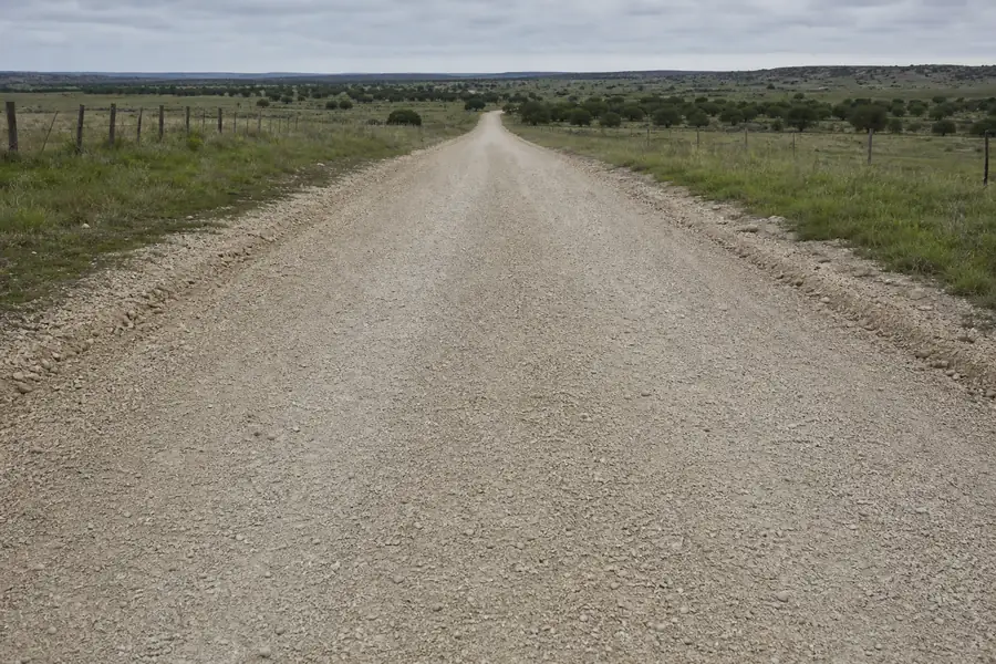 Freshly graded caliche ranch road with a crowned surface stretching across Texas grassland