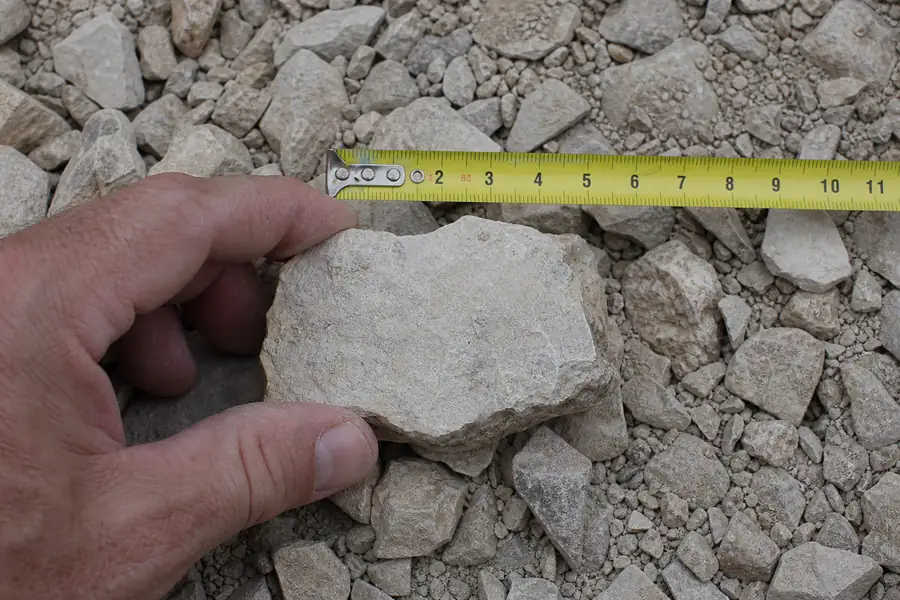 Hand holding #57 limestone stone against a tape measure
