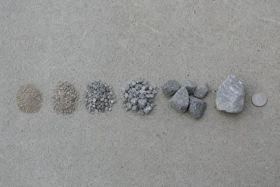 Row of gravel samples from fines to 2 inch stone next to a coin for scale