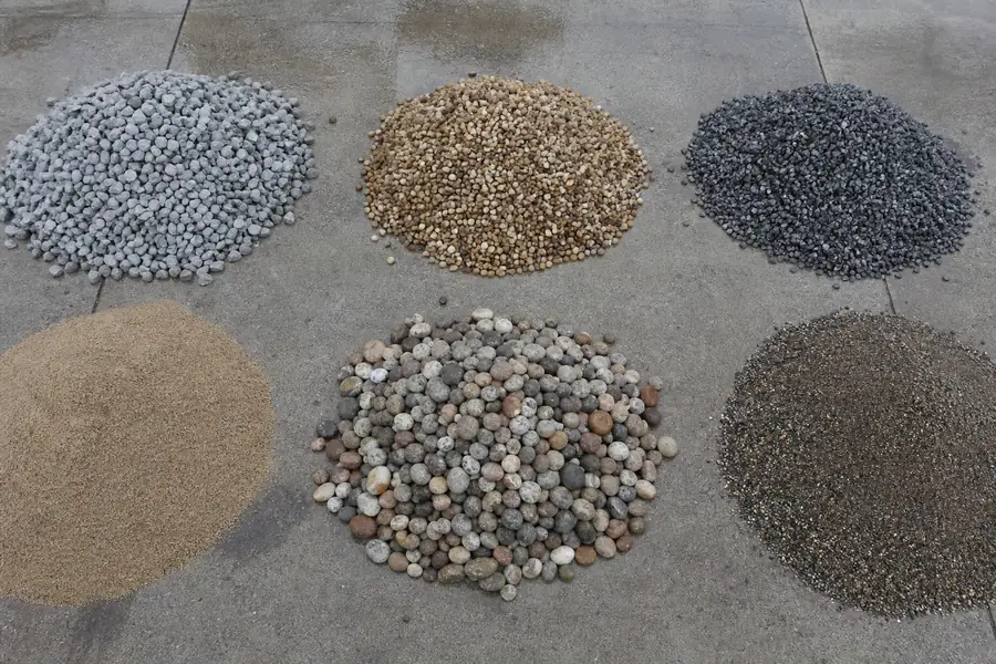 Six labelled piles of different gravel types laid out on a concrete pad